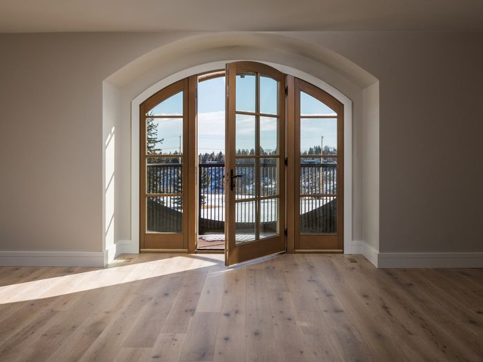 A room with arched french doors onto a garden, floored in a light tone that carries the daylight