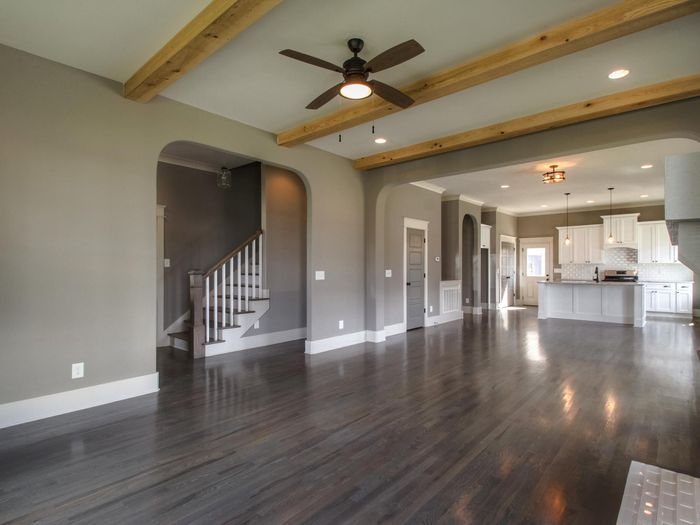 A living room with exposed ceiling beams, the floor carrying through an open sightline to the kitchen beyond