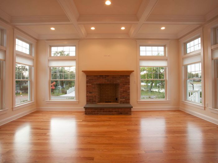 A living room with a coffered ceiling and bay windows, floored wall to wall in warm oak