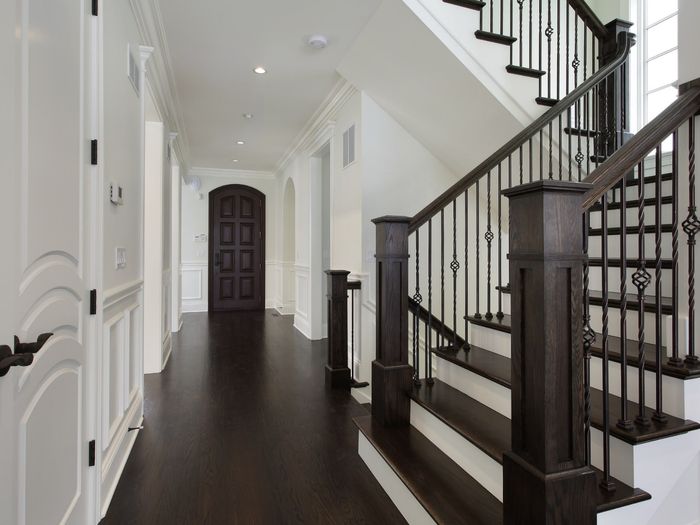 A dark staircase with iron spindles against white wainscoting, matched to the hall floor at its foot