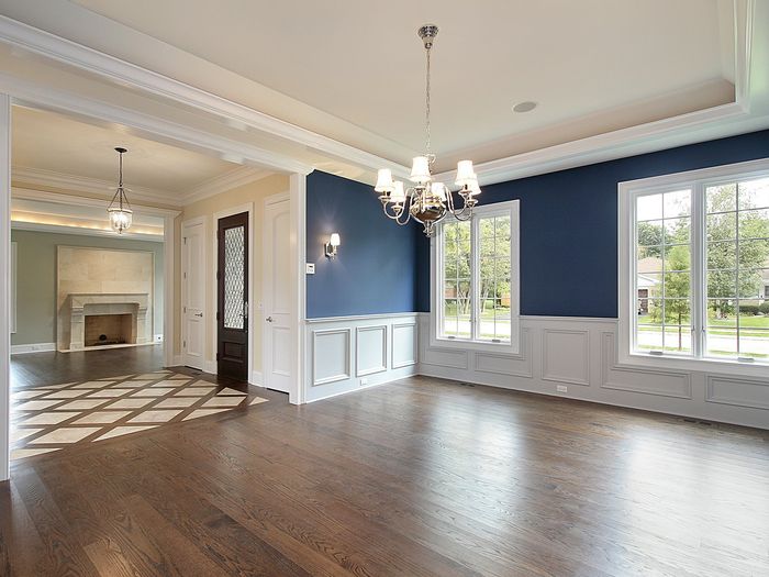 A dining room with wainscoting and a navy accent wall, the floor reading mid-brown in the room own daylight