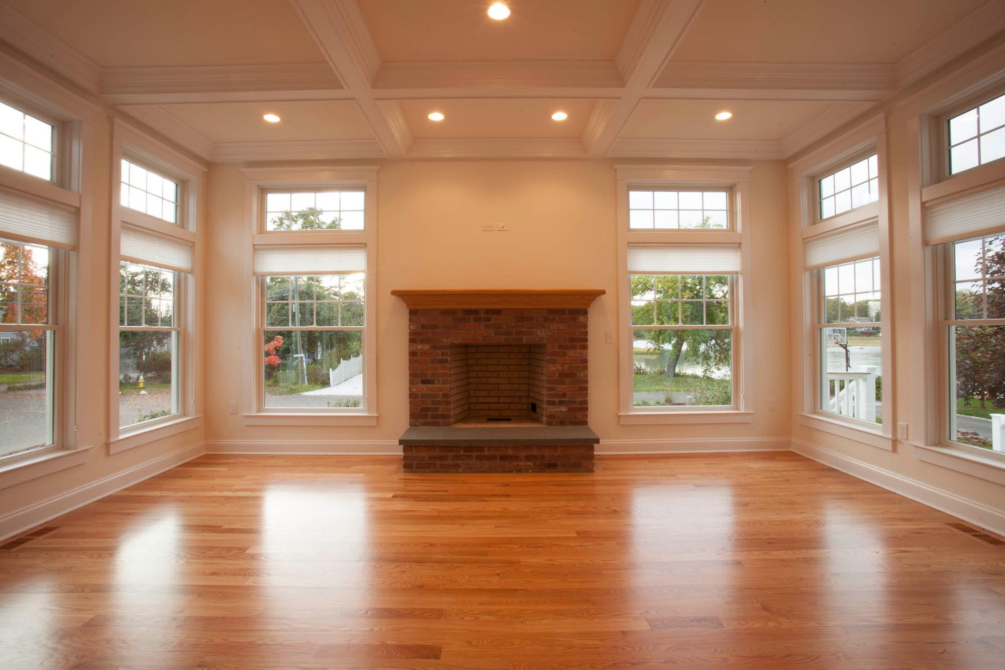 A finished Referral Flooring job: a coffered-ceiling living room floored wall to wall in warm oak, with the bay window light running down the length of the plank