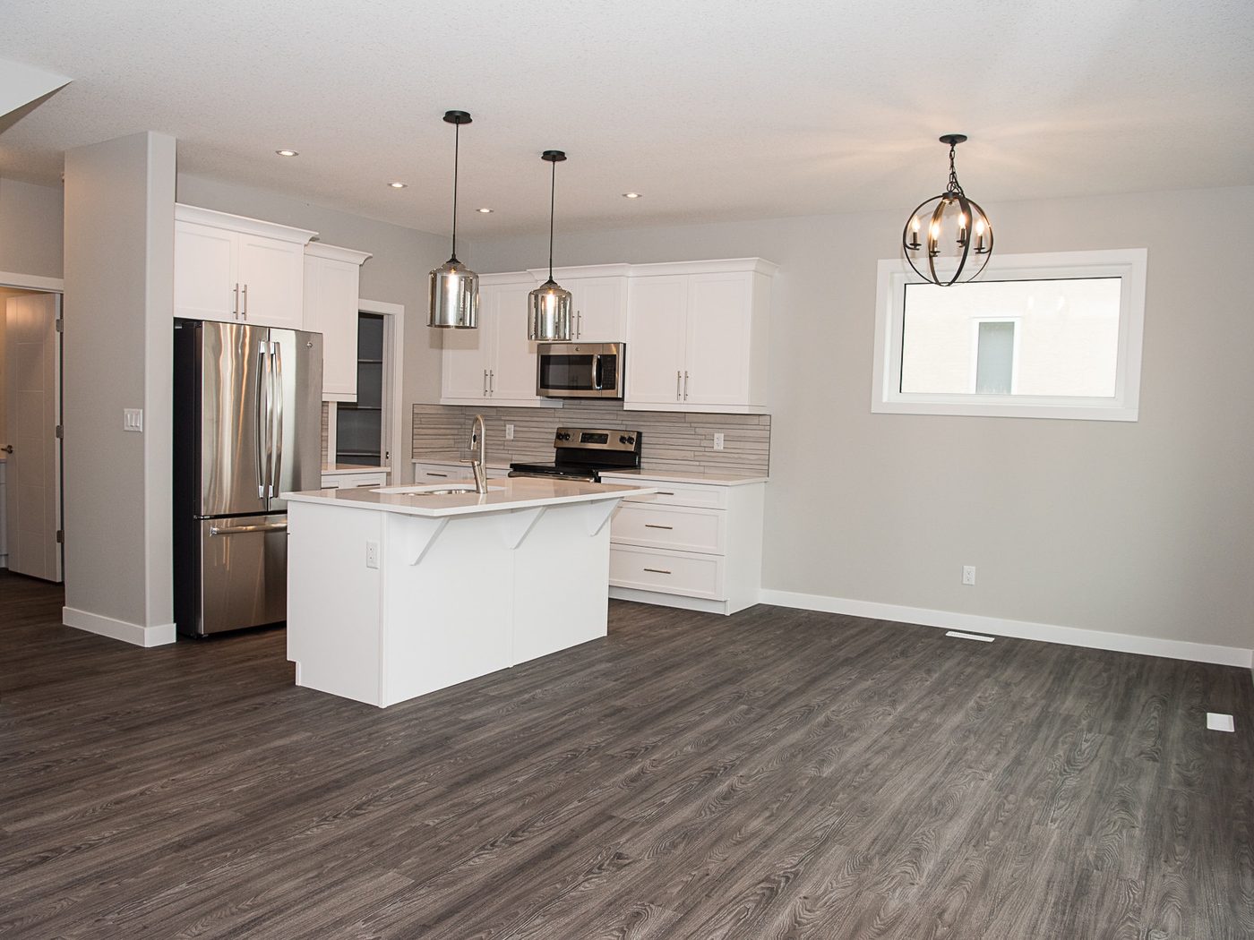 A kitchen floored in one continuous run under the island and appliances, with no transition strip at the doorways