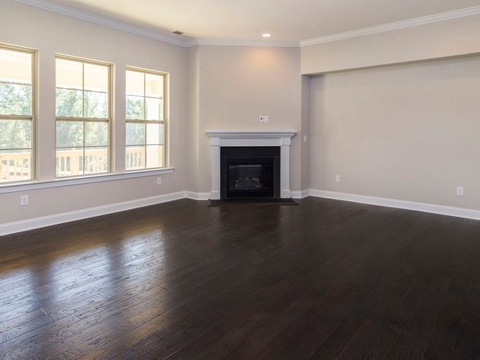 A living room with a fireplace and tall windows, floored in a dark tone with the baseboard refitted