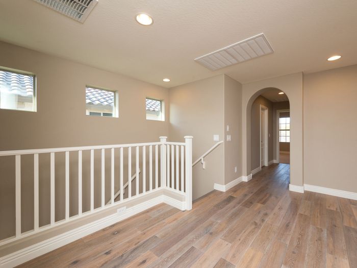 An upstairs landing with a white painted railing, floored continuously with the rooms it serves