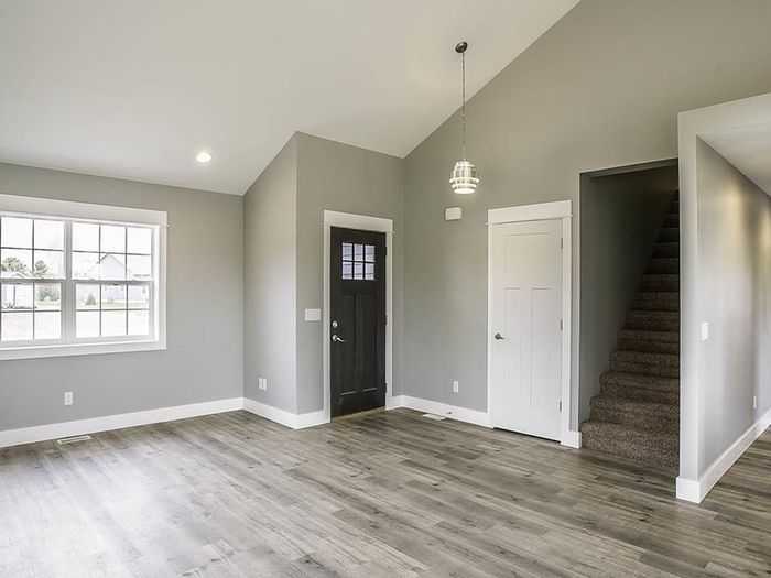 A living room with a vaulted ceiling and a staircase to one side, floored in a wide plank