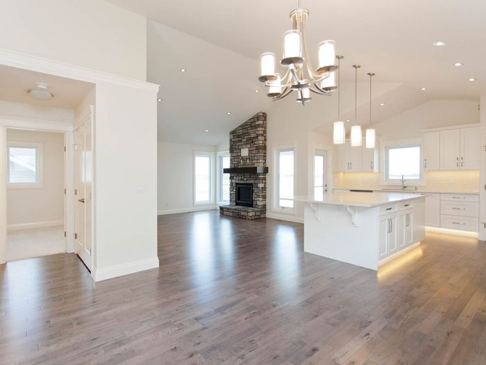 A white kitchen with an island and pendant lighting, opening onto a dining area on one continuous floor